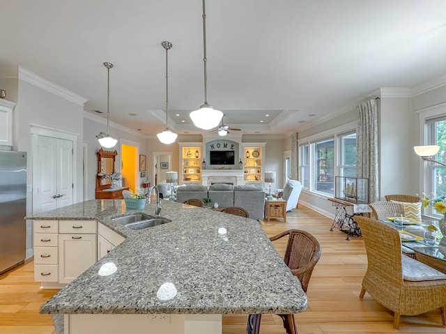 kitchen with light wood-type flooring, stainless steel refrigerator, crown molding, a center island with sink, and a sink