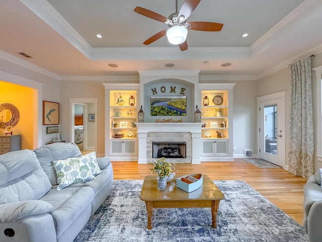 living area with a raised ceiling, light wood finished floors, ceiling fan, and ornamental molding