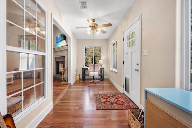 foyer entrance with ceiling fan, wood-type flooring, a tile fireplace, and a healthy amount of sunlight