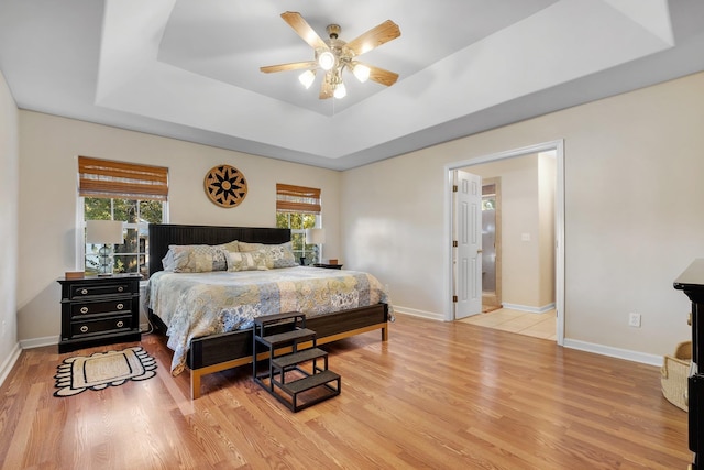 bedroom with light wood-type flooring, ceiling fan, and a raised ceiling