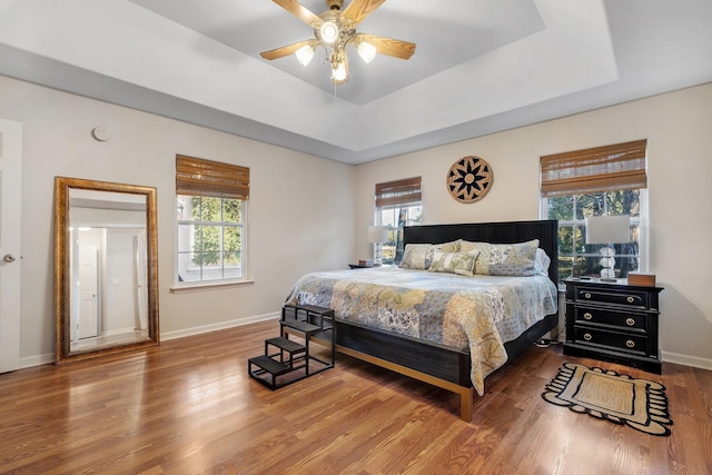 bedroom featuring multiple windows, hardwood / wood-style flooring, ceiling fan, and a raised ceiling