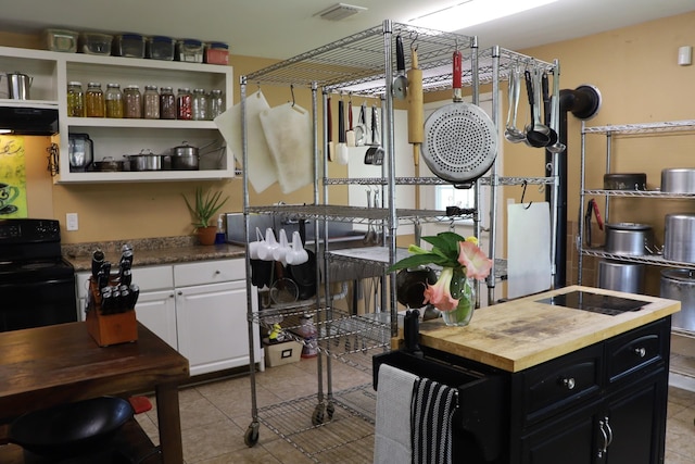 kitchen with white cabinetry, black range with electric cooktop, extractor fan, and light tile patterned flooring