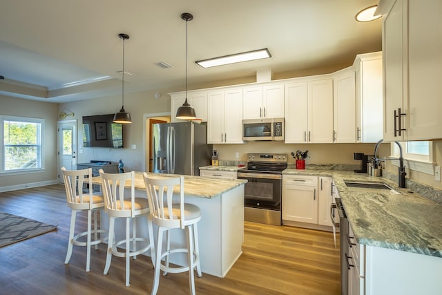 kitchen featuring sink, white cabinetry, decorative light fixtures, appliances with stainless steel finishes, and a kitchen island