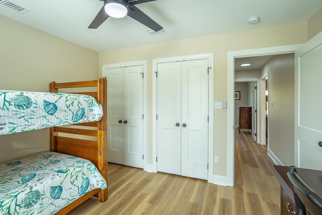 bedroom featuring ceiling fan, light hardwood / wood-style flooring, and two closets