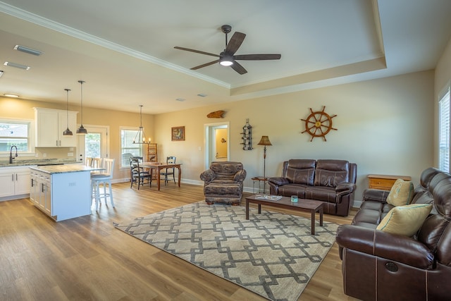 living room with a raised ceiling, crown molding, sink, and light hardwood / wood-style flooring