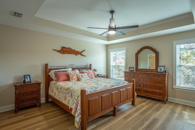 bedroom with ceiling fan, wood-type flooring, and a raised ceiling