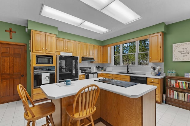 kitchen featuring black appliances, a breakfast bar area, sink, a kitchen island, and backsplash