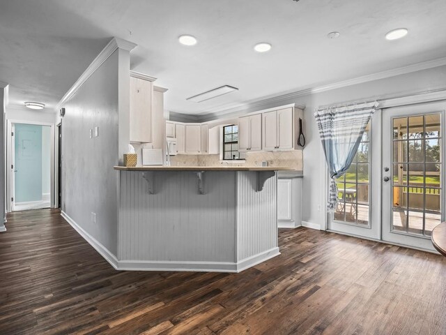 kitchen with dark hardwood / wood-style flooring, kitchen peninsula, crown molding, a kitchen bar, and white cabinets