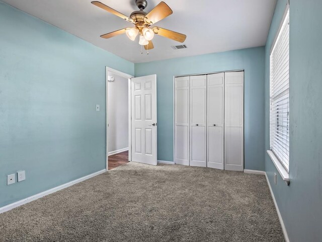 unfurnished bedroom with ceiling fan, a closet, and dark carpet