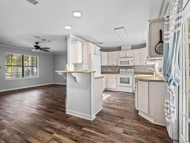 kitchen with a breakfast bar, white appliances, dark wood-type flooring, crown molding, and kitchen peninsula