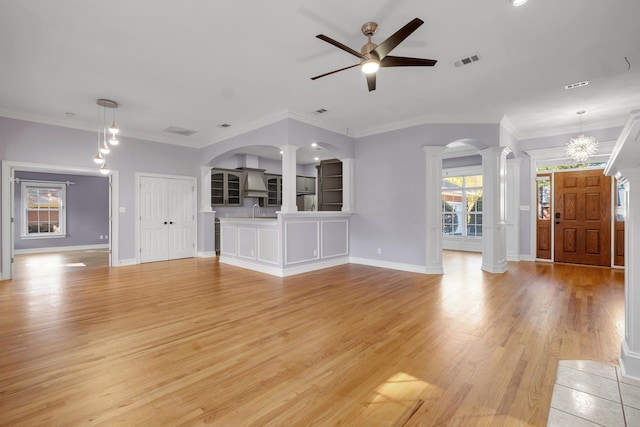 unfurnished living room with ceiling fan with notable chandelier, light wood-type flooring, ornamental molding, and decorative columns