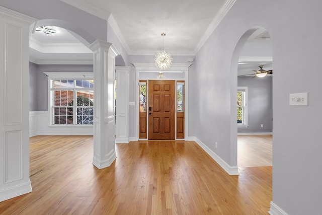 entrance foyer with ornamental molding, light hardwood / wood-style flooring, ceiling fan with notable chandelier, and ornate columns