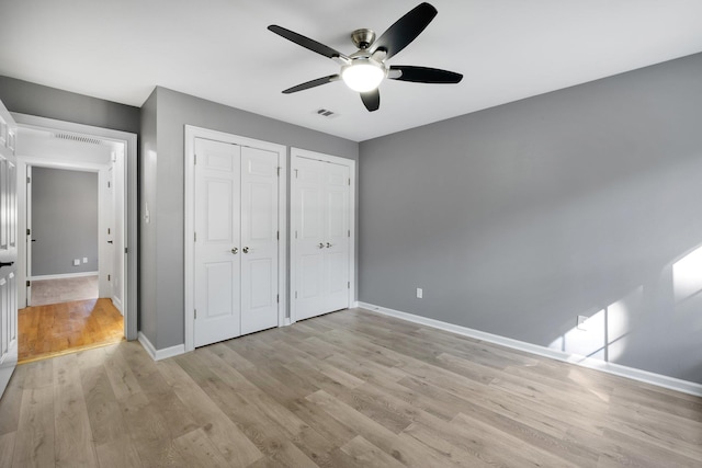 unfurnished bedroom with two closets, ceiling fan, and light hardwood / wood-style flooring