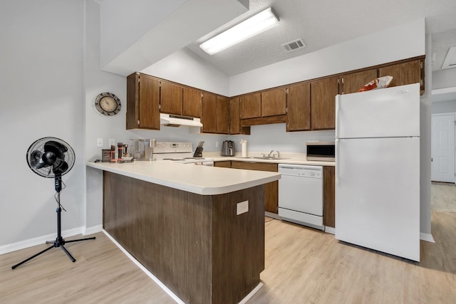 kitchen with light hardwood / wood-style floors, kitchen peninsula, a textured ceiling, white appliances, and vaulted ceiling