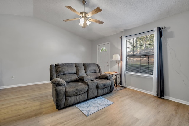 living room with a textured ceiling, light hardwood / wood-style flooring, ceiling fan, and vaulted ceiling