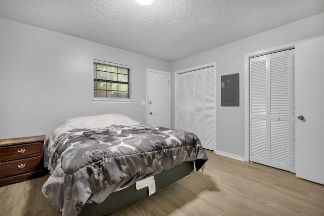 bedroom featuring electric panel, a textured ceiling, two closets, and light hardwood / wood-style floors