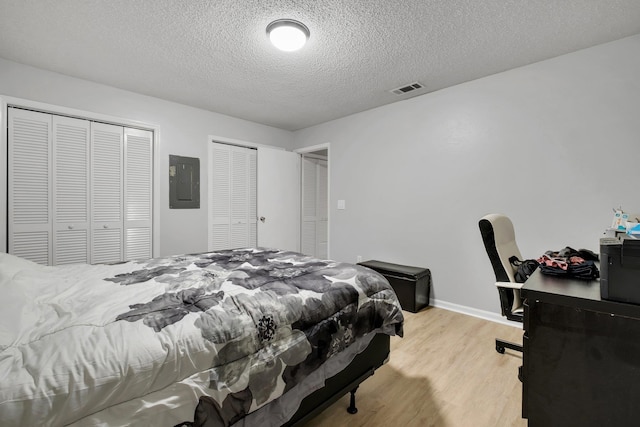 bedroom with multiple closets, light hardwood / wood-style floors, electric panel, and a textured ceiling