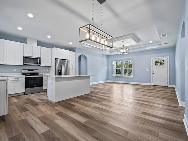 kitchen with stainless steel appliances, decorative light fixtures, hardwood / wood-style flooring, white cabinets, and a center island