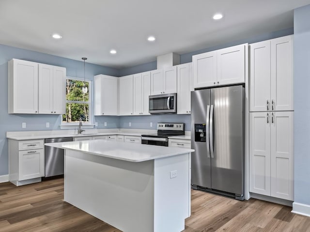 kitchen with sink, stainless steel appliances, hardwood / wood-style floors, decorative light fixtures, and white cabinets