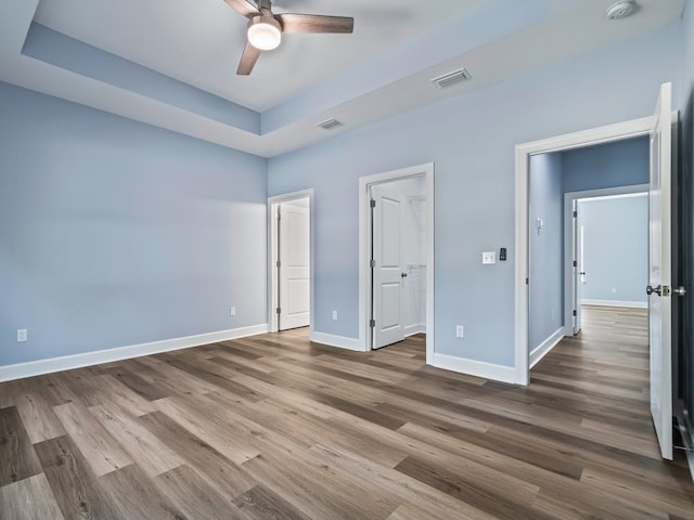 unfurnished bedroom with a raised ceiling, ceiling fan, and wood-type flooring