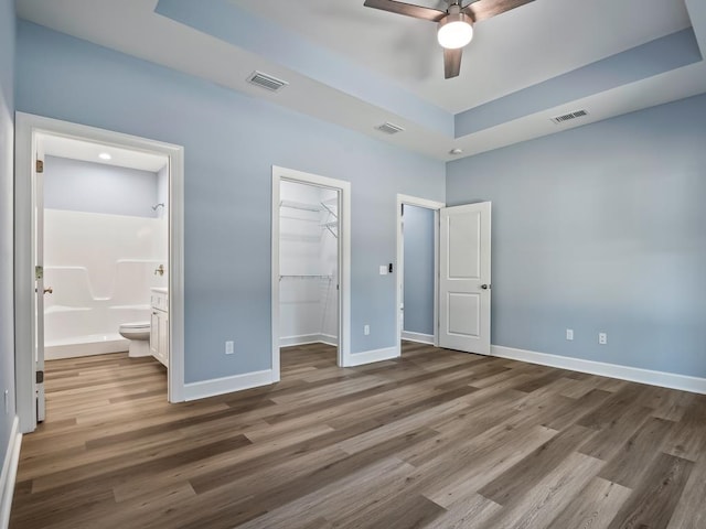 unfurnished bedroom featuring dark hardwood / wood-style flooring, a walk in closet, ensuite bath, ceiling fan, and a closet