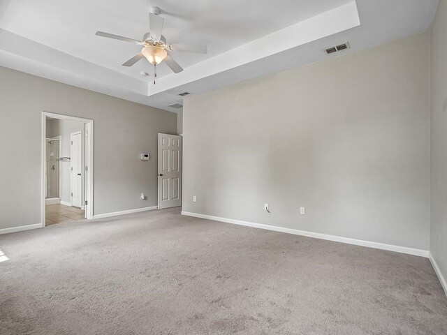 empty room with a tray ceiling, light colored carpet, and ceiling fan