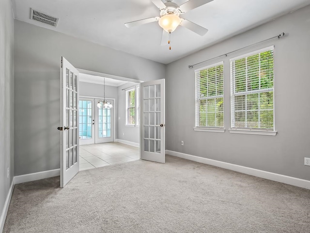 carpeted spare room with french doors, ceiling fan with notable chandelier, and plenty of natural light