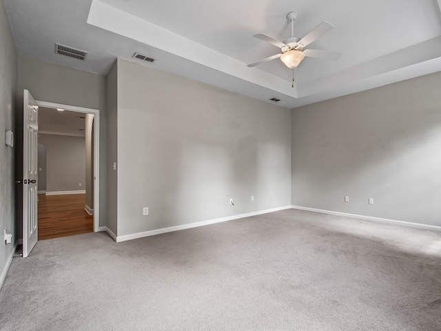 carpeted spare room with ceiling fan and a raised ceiling