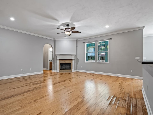 unfurnished living room with ceiling fan, a tile fireplace, light hardwood / wood-style flooring, and crown molding