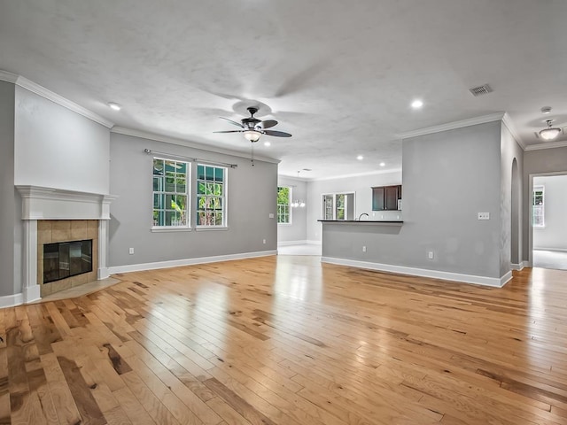 unfurnished living room with light wood-type flooring, a tiled fireplace, ceiling fan, and ornamental molding