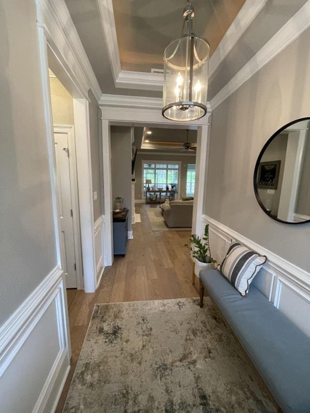 hall with crown molding, a tray ceiling, a chandelier, and light wood-type flooring