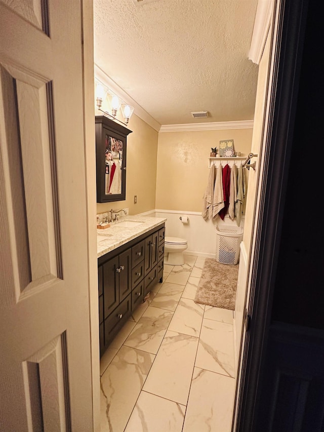 bathroom featuring vanity, toilet, ornamental molding, and a textured ceiling