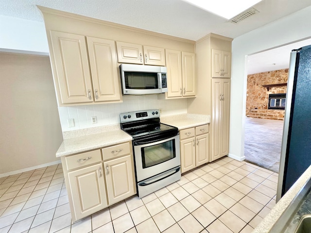 kitchen with appliances with stainless steel finishes, a textured ceiling, light tile patterned floors, a fireplace, and decorative backsplash