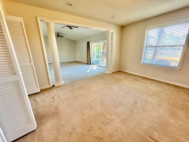 empty room with decorative columns, a textured ceiling, light carpet, and ceiling fan