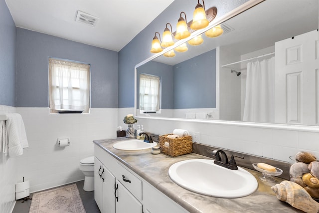 bathroom with vanity, toilet, a shower with shower curtain, and tile walls