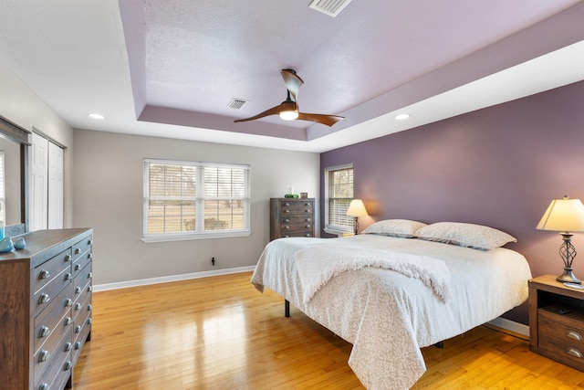 bedroom featuring light hardwood / wood-style floors, a raised ceiling, and ceiling fan