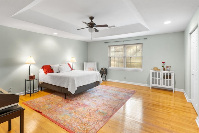 bedroom with hardwood / wood-style flooring, ceiling fan, a raised ceiling, and a closet