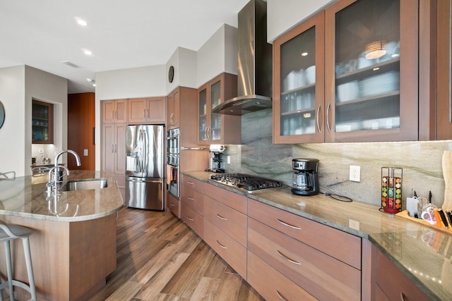 kitchen with appliances with stainless steel finishes, hardwood / wood-style floors, sink, a breakfast bar area, and wall chimney exhaust hood