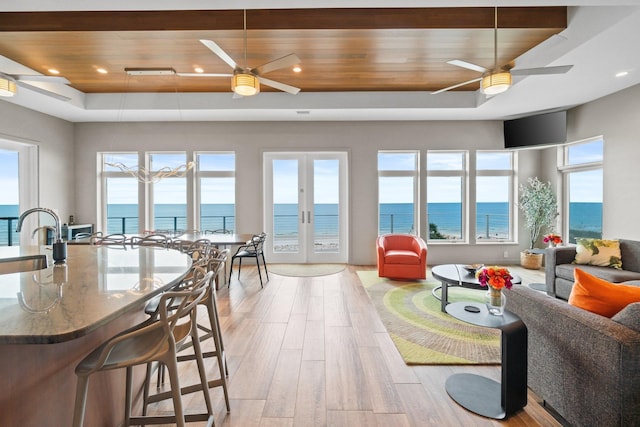 living room with wooden ceiling, a healthy amount of sunlight, a water view, and light hardwood / wood-style flooring