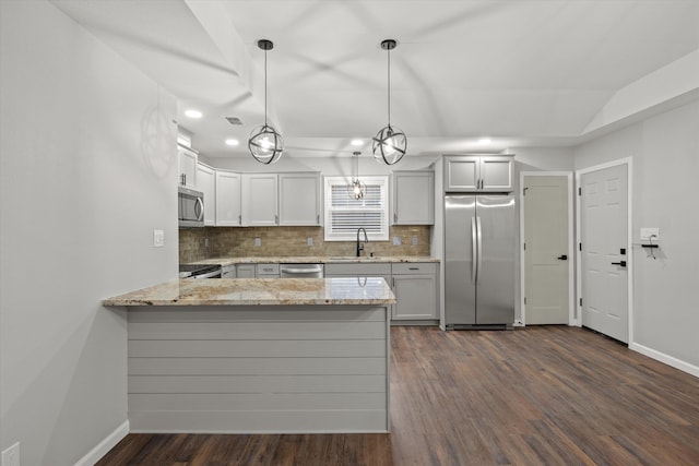 kitchen featuring a sink, light stone counters, appliances with stainless steel finishes, a peninsula, and decorative backsplash