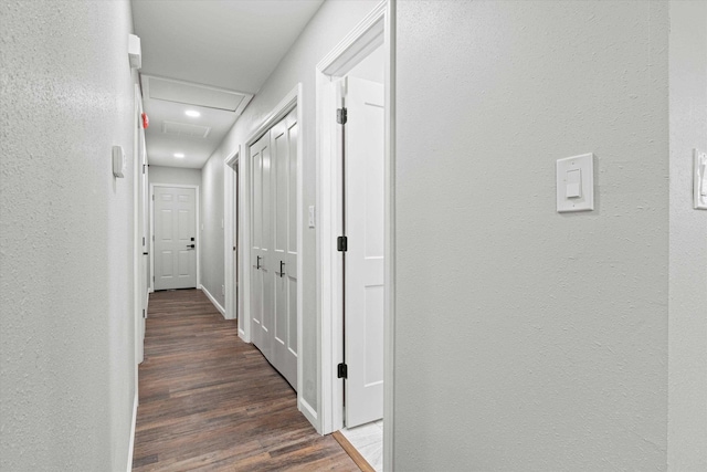 corridor featuring attic access, wood finished floors, and a textured wall