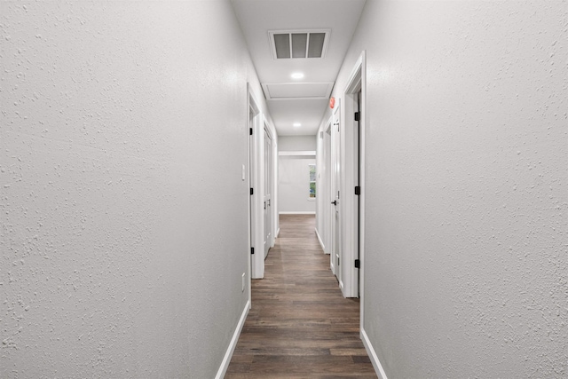 hall featuring wood finished floors, a textured wall, visible vents, and baseboards