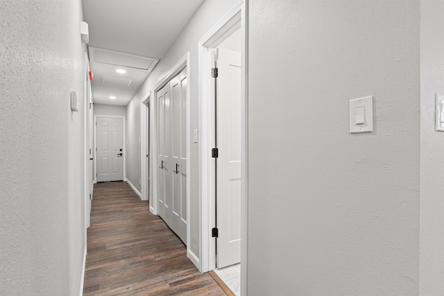 hallway featuring attic access, wood finished floors, and a textured wall