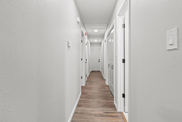 corridor with baseboards, wood finished floors, and a textured wall