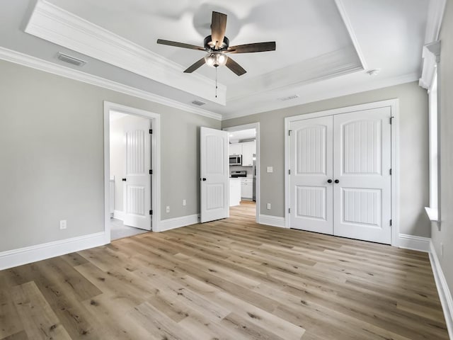 unfurnished bedroom featuring light hardwood / wood-style flooring, a raised ceiling, ceiling fan, and crown molding