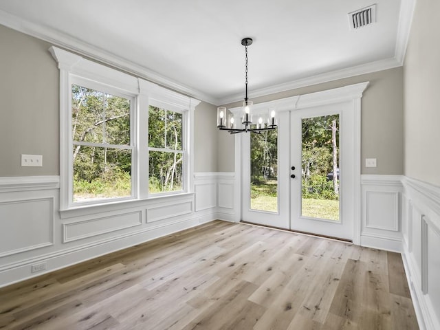 unfurnished dining area featuring french doors, light wood-type flooring, an inviting chandelier, and ornamental molding