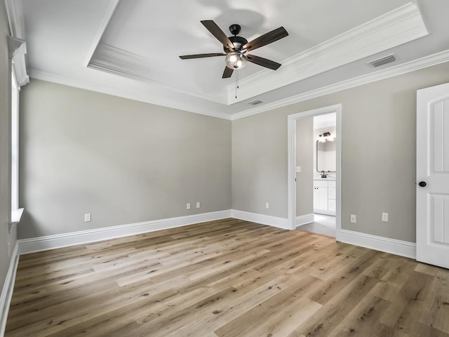 unfurnished bedroom featuring ceiling fan, a raised ceiling, ensuite bathroom, wood-type flooring, and ornamental molding