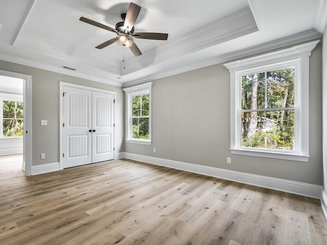 unfurnished bedroom featuring a raised ceiling, multiple windows, ceiling fan, and light wood-type flooring