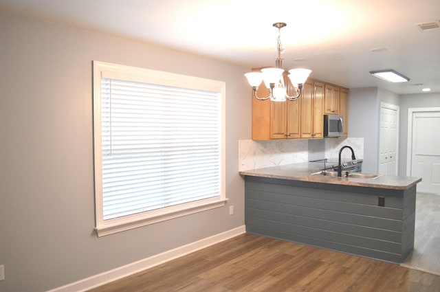 kitchen with sink, a notable chandelier, kitchen peninsula, pendant lighting, and decorative backsplash