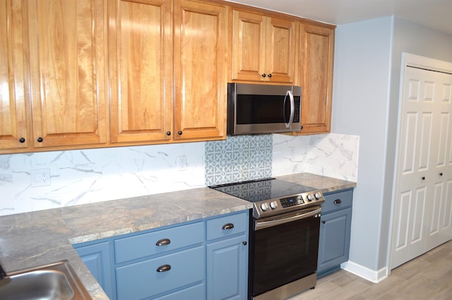 kitchen featuring tasteful backsplash, dark stone countertops, stainless steel appliances, and light hardwood / wood-style floors